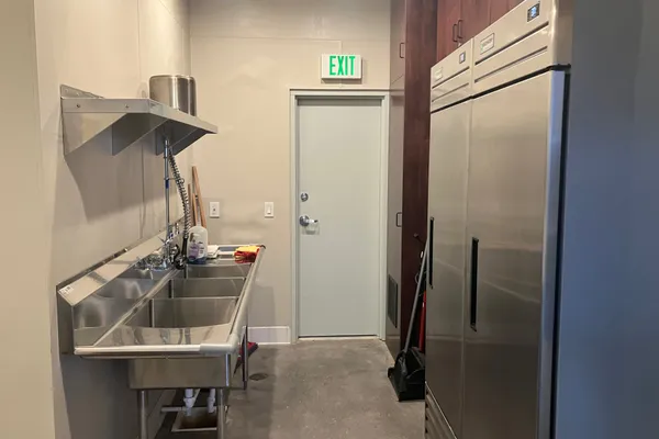 Kitchen walk-in area with commercial sinks, refrigerators, and stainless-steel shelving